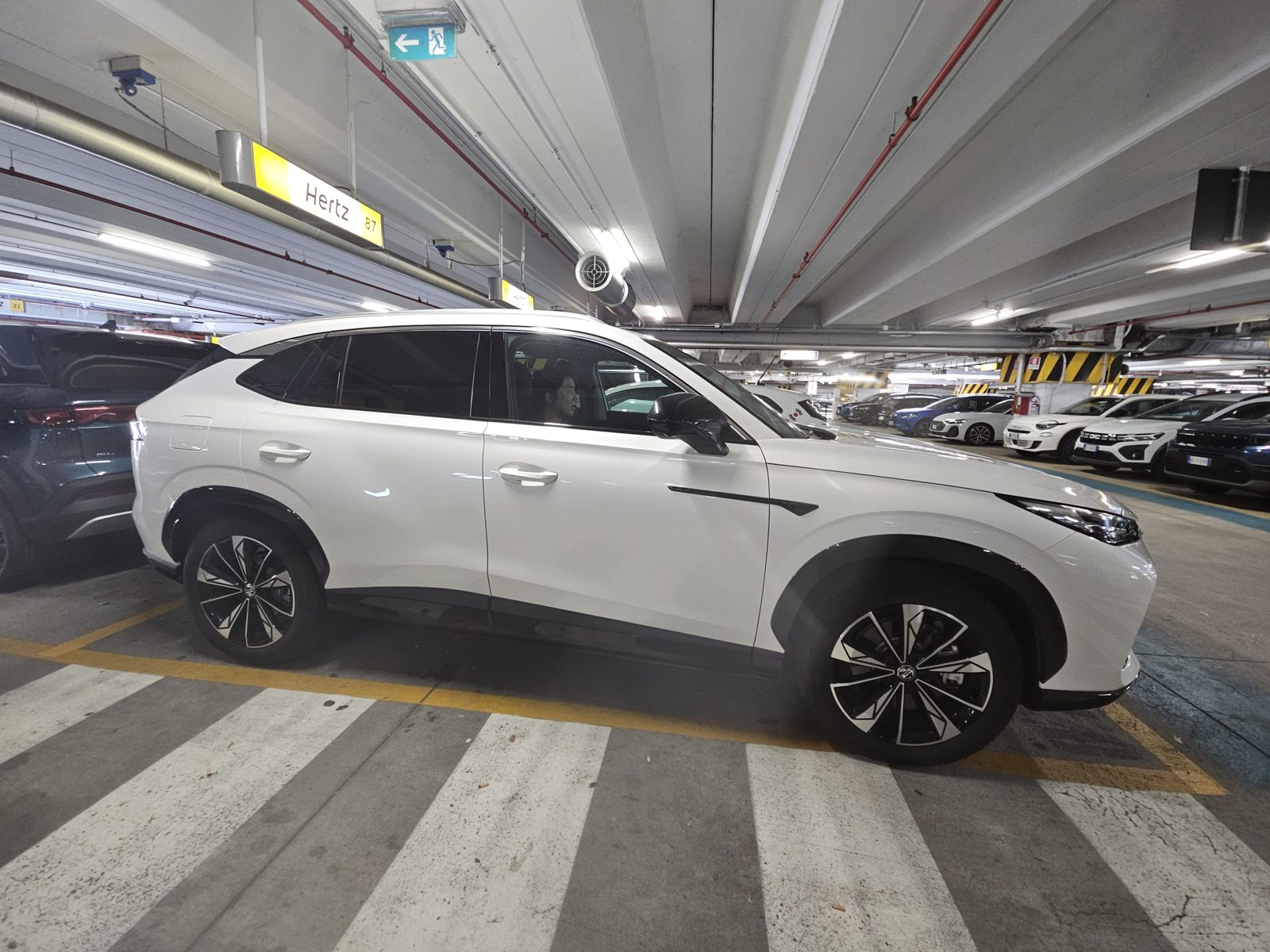 White MG HS hybrid SUV rental car from Hertz in a Milan airport car park